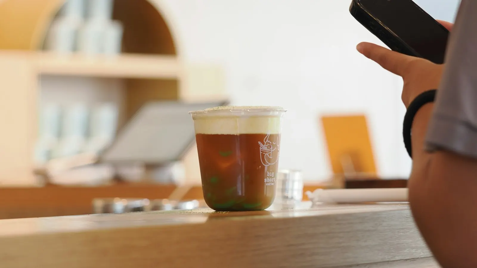 A customer holding a smartphone at a café counter
