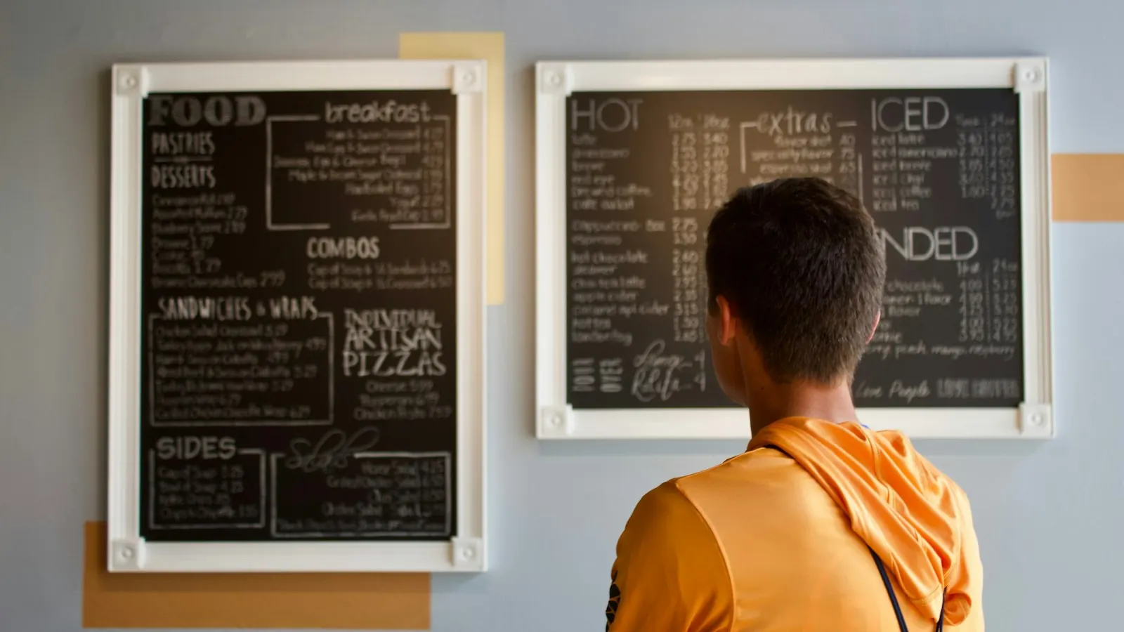 A man reading the menu boards on the wall of a café